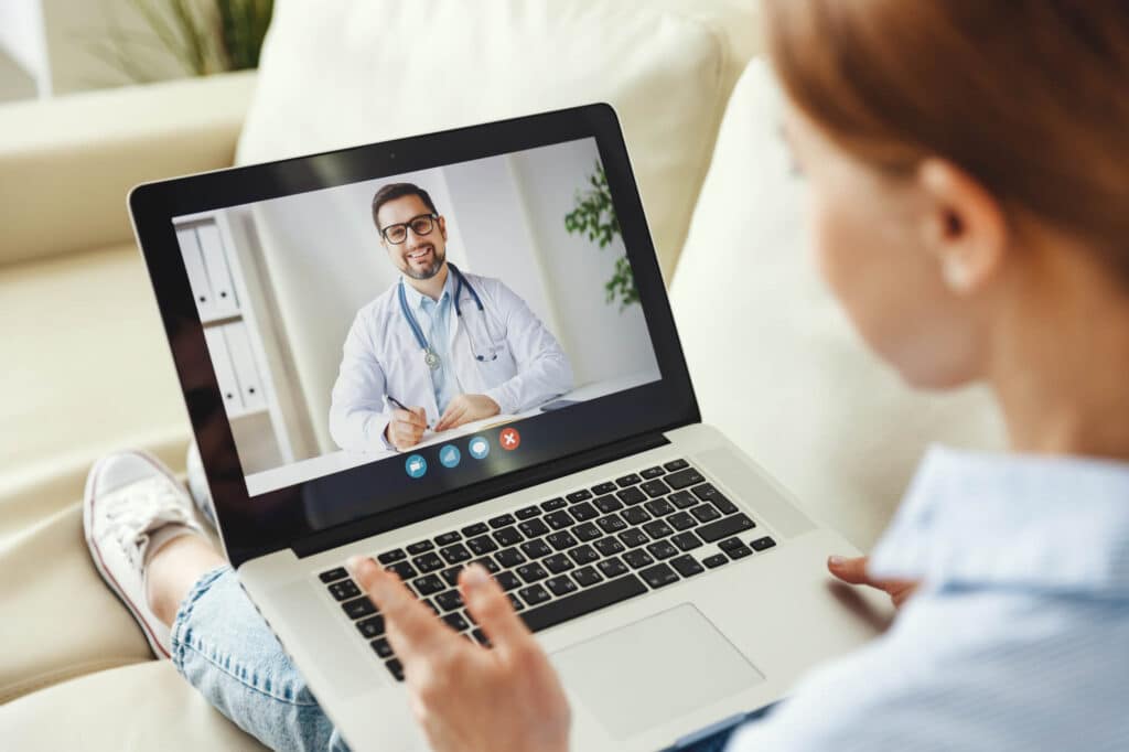 A person is engaging in a video call with a doctor displayed on a laptop screen, highlighting the importance of remote patient monitoring in modern healthcare.