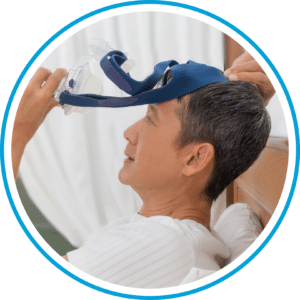 A person lies in bed, holding a CPAP mask near their face with a neutral expression, their trusted Sleep Buddy.
