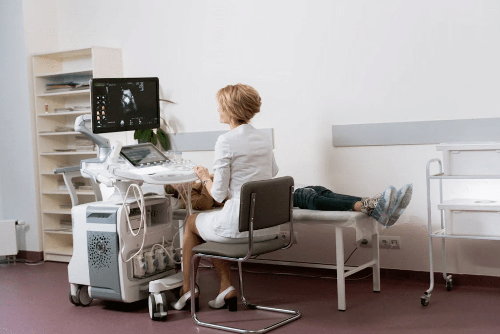 A medical professional conducts an ultrasound on a patient lying on an examination bed, focusing intently on the monitor displaying the images. The procedure aligns with Chronic Care Management protocols, ensuring comprehensive care for ongoing health needs.