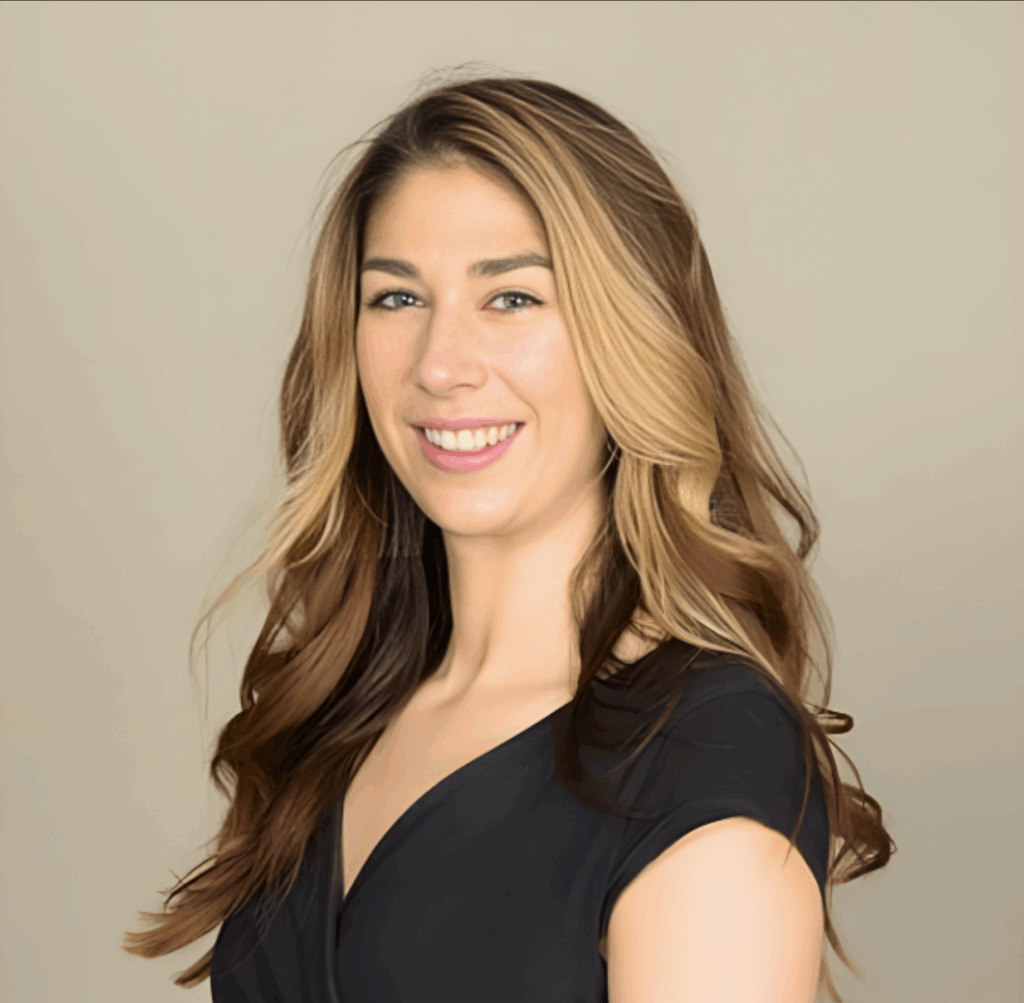 A woman with long, wavy, light brown and blonde hair wearing a black top stands against a plain beige background, smiling confidently at the camera—radiating the positivity found in success stories.