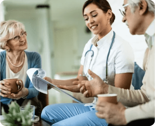 A healthcare professional discusses documents with two older adults. They are seated with coffee cups, engaging in a conversation about strategies that could potentially double your revenue while focusing on well-being and peace of mind.
